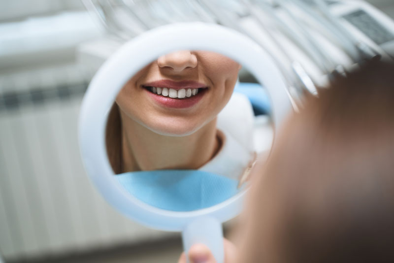 Lower half of attractive woman's face reflected in mirror after a dental procedure at Pearl Dental Associates.