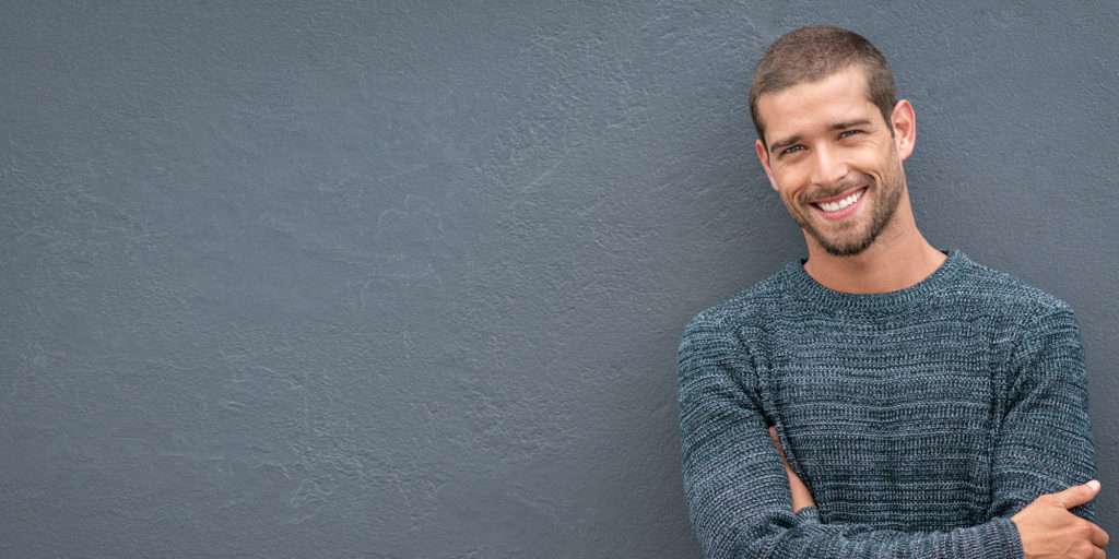 Smiling man with teeth whitening standing in front of a blue wall.