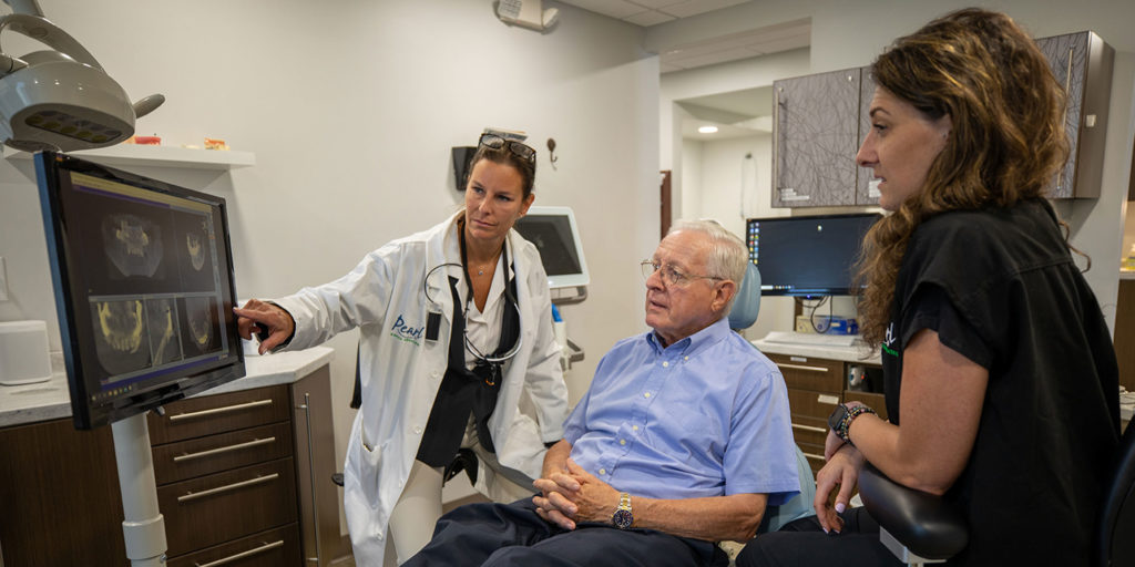 Dr Theresa Salem with staff and elderly patient going over dental implant cbct scan on a monitor.